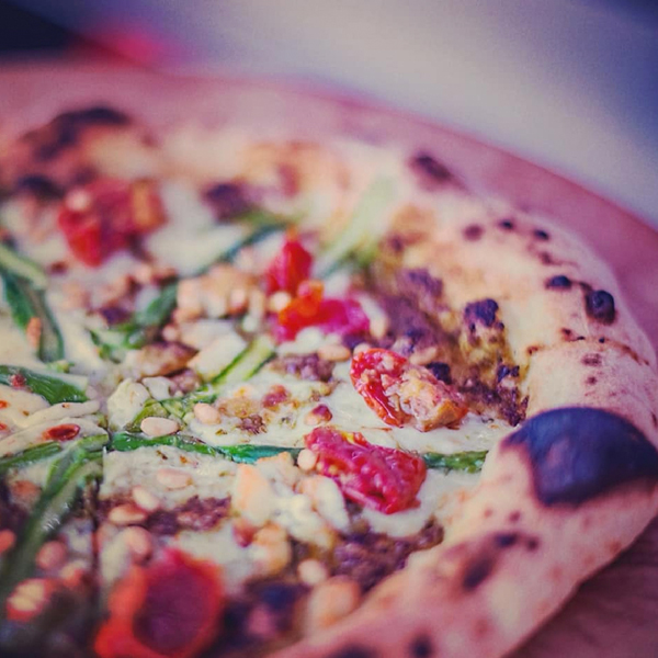 Close up of a pizza topped with tomatoes, courgette, cheese and pine nuts